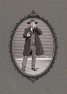 An old timey black and white photo of a man dressed like an old gunslinger